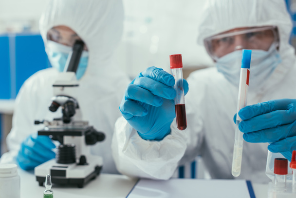 foyer sélectif du biochimiste tenant des éprouvettes avec échantillon de liquide et de sang près d'un collègue regardant au microscope
 - Photo, image