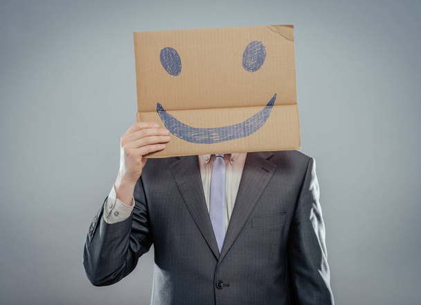 Одягніть усміхнене обличчя. Чоловік тримає картонний папір зі смайликом, надрукованим як концепція щастя та радості
. - Фото, зображення