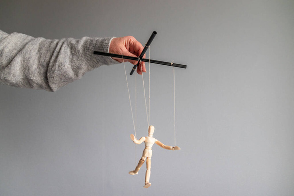 La mano humana sostiene una muñeca de madera en el tendedero sobre un fondo gris con lugar para el texto. Concepto de metáfora de poder
 - Foto, imagen