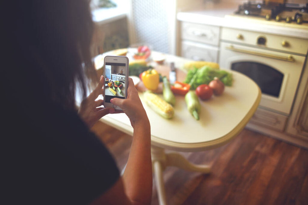 Kız yemek pişirmek için akıllı telefon malzemeleriyle fotoğraf çekiyor. Taze sebze fotoğrafı. Mutfak blogu. Yaşam tarzı. Sağlıklı beslenme. Bağışıklığı güçlendiriyor. - Fotoğraf, Görsel