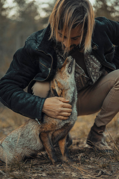 Bearded young man with a wild fox in the mountains - Photo, Image