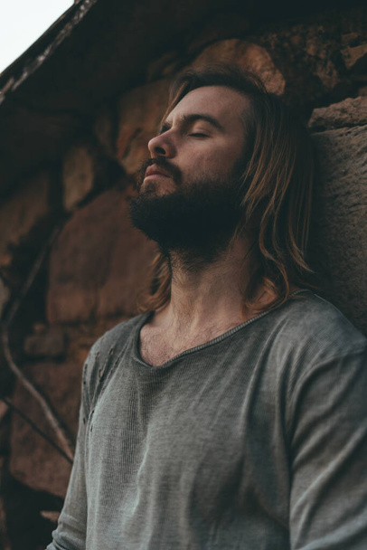 Bearded young man meditating on the farmhouse wall - Фото, зображення