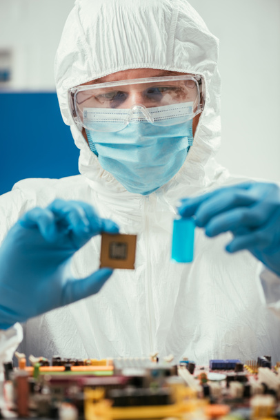 foco selectivo del ingeniero que sostiene el microchip y el envase de cristal con el líquido azul cerca de la placa madre de la computadora
 - Foto, imagen
