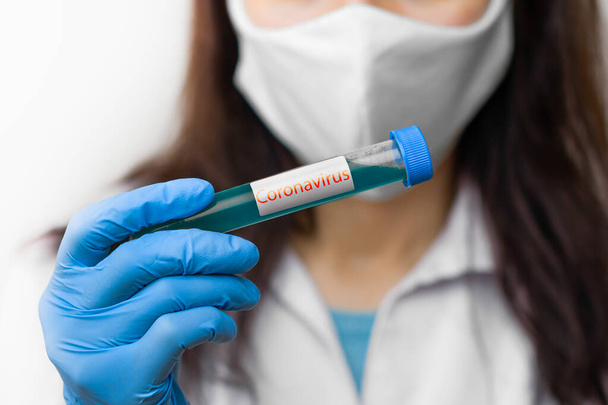 Testovací zkumavka s vakcínou proti koronaviru, 2019-nCoV, SARS-nCov, COVID-19 v ruce vědec s ochrannou maskou a modrými rukavicemi - Fotografie, Obrázek