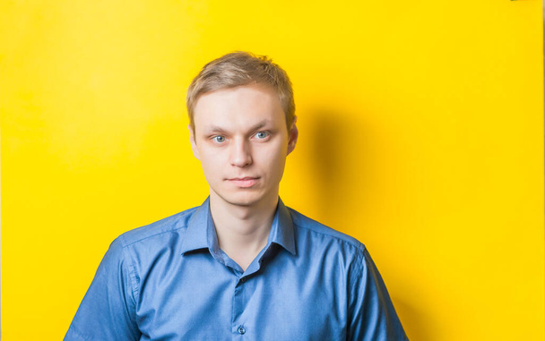 Serious young blond man in a blue shirt on a yellow background. Photo Shoot. - Foto, immagini