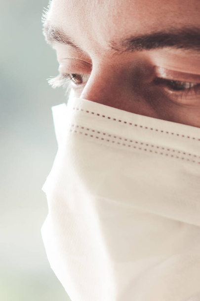 Vertical photo of a young bearded white man with a medical face mask during coronavirus quarantine. The front part of the face lightly blurred. Coronavirus, COVID-19 outbreak. Doctor, nurse concept. - Foto, Bild