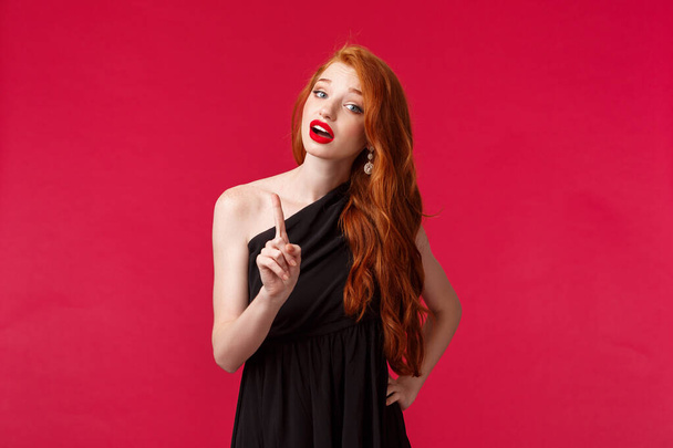 Fashion, luxury and beauty concept. Portrait of bossy good-looking young redhead woman in black dress give warning, shaking finger in caution scolding someone, give stop sign, patronising - Fotoğraf, Görsel