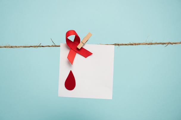 Card with blood drop and red ribbon on rope with pin isolated on blue, concept of hemophilia  - Fotó, kép
