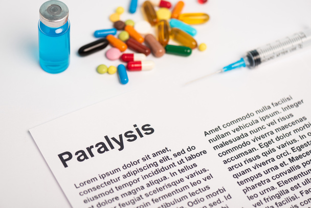 Paper with paralysis lettering near jar, syringe and pills on white background - Foto, Imagem