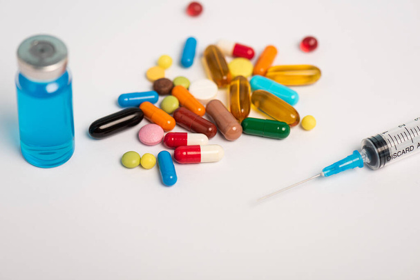 Close up view of colorful pills, syringe and jar of vaccine on white surface - Valokuva, kuva