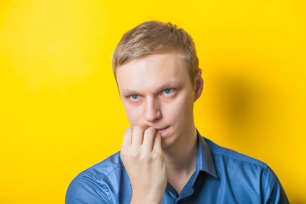 Blond young man holding his finger to his temple, thinking what to do. Close portrait. Gesture. Isolated yellow background. photo - Photo, Image