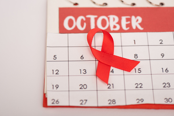 Nahaufnahme des roten Bandes der Hilfsmittel Bewusstsein auf Kalender mit Oktober Monat isoliert auf grau - Foto, Bild