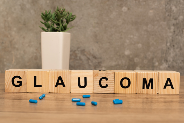 Selective focus of glaucoma lettering on cubes with pills and plant on wooden table on grey background - Foto, afbeelding