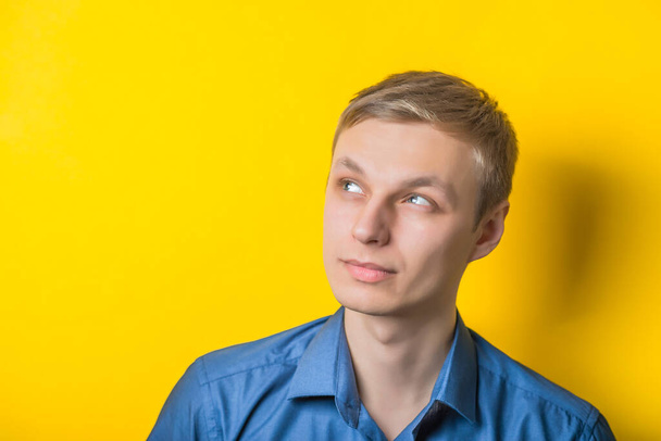 Young man close-up in a blue shirt on a yellow background, thoughtful, artful, something planned. Mimicry. Gesture. photo Shoot - Foto, immagini