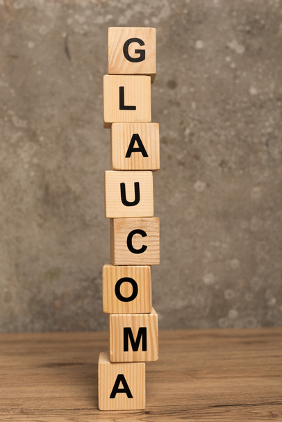 Stacked cubes with glaucoma lettering on wooden table on grey background - Photo, Image