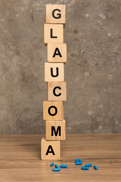 Gestapelde blokjes met glaucoom belettering en pillen op houten tafel op grijze achtergrond - Foto, afbeelding