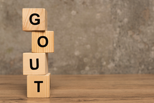 Stacked cubes with gout lettering on wooden table on grey background - Photo, Image