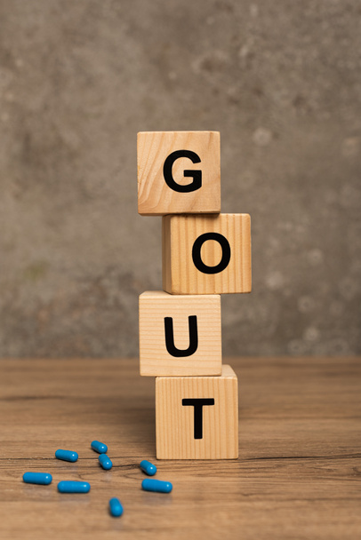 Selective focus of wooden cubes with gout lettering pills on wooden table on grey background - Photo, Image