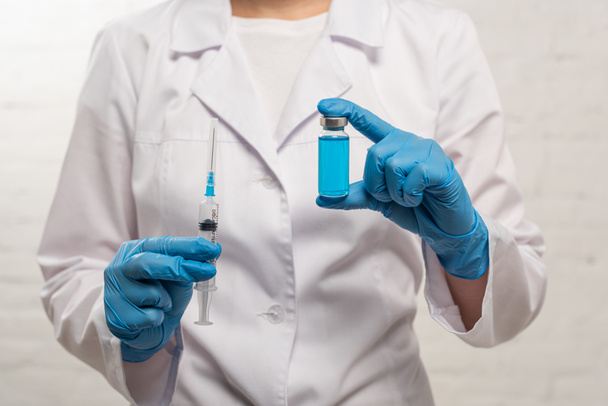 Vista ritagliata del medico che tiene siringa e vaso di vaccino su sfondo bianco
 - Foto, immagini
