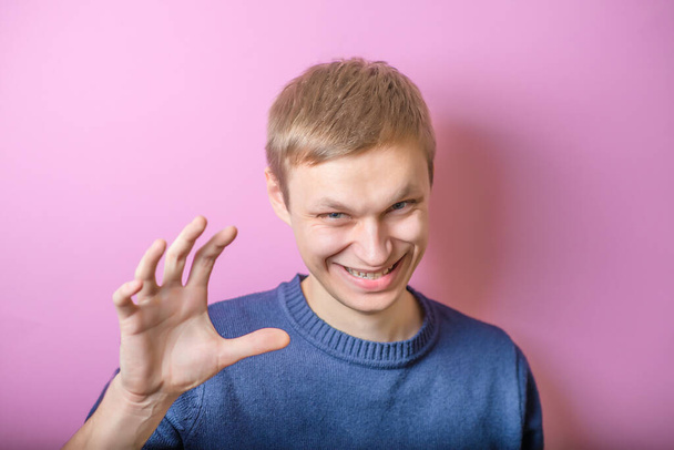 Young man scared smiling, joking. Gesture. On a purple background. - Foto, afbeelding