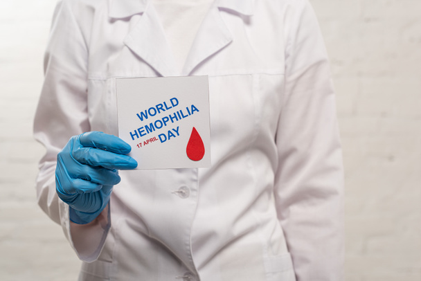 Gewassen mening van arts holding card met wereld hemofilie dag op witte achtergrond - Foto, afbeelding