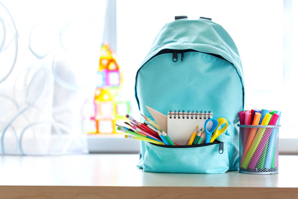 Blue school backpack with school supplies on table over children room interior in sunny day. Back to school concept. - Foto, afbeelding