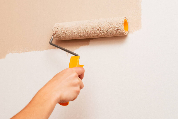 Réparation dans la maison. Un homme peint les murs avec un rouleau de couleur beige
 - Photo, image