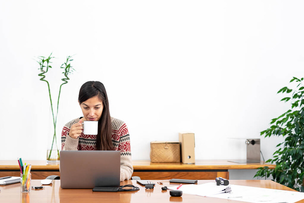 Jovem freelancer trabalhando em um escritório doméstico improvisado conectado à internet com um laptop e um telefone durante o período de confinamento global
 - Foto, Imagem