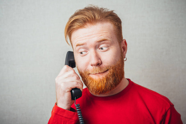 closeup portrait of Young hipster red bearded Man talking on corded retro phone  - Foto, afbeelding