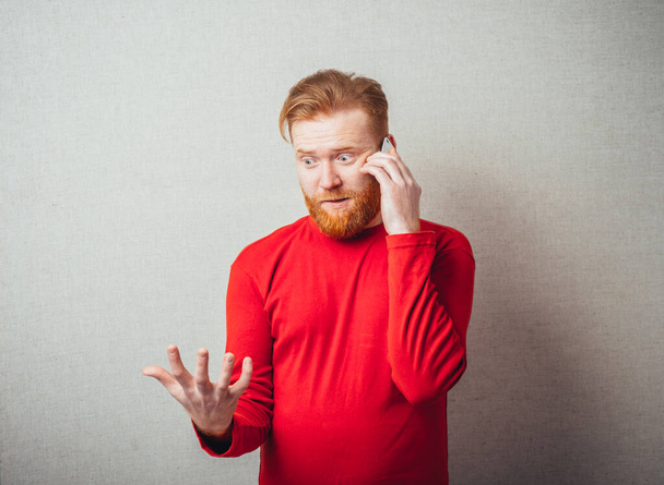on a gray background, bearded man in a red shirt talking on the phone - Foto, immagini