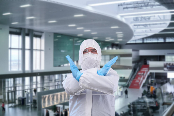 людина епідеміолог в одноразовому анти-епідемічному антибактеріальному ізоляційному костюмі показує заборонний жест проти внутрішньої частини аеропорту або поїзда статио
 - Фото, зображення