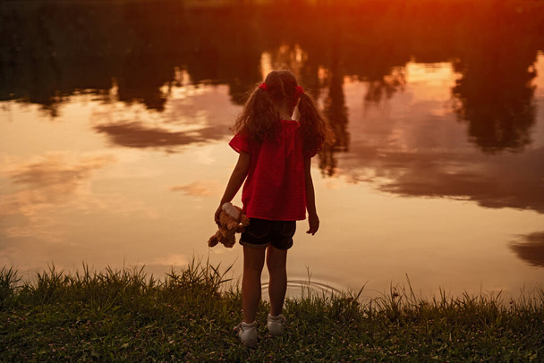 Lonely little girl standing on shore of lake - Foto, afbeelding