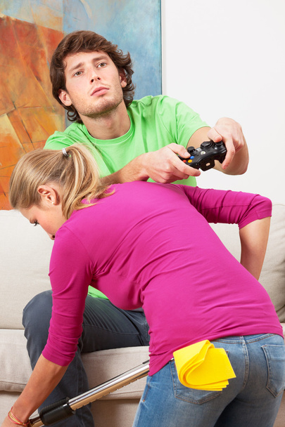Woman cleaning the house and her husband with console - Фото, изображение