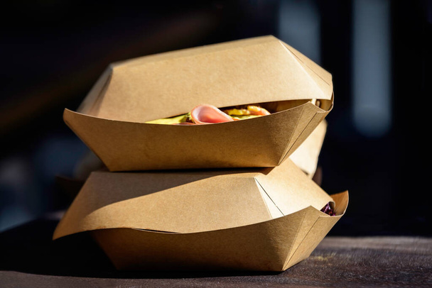 Dos cajas de cartón marrón para llevar expuestas en una mesa de madera en un mercado callejero de alimentos, listas para la venta y comen alimentos saludables
 - Foto, imagen