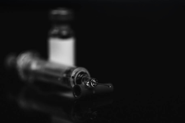 Fechar o frasco para injetáveis médico para injetáveis com uma seringa e ampola sobre fundo preto. Foto em preto e branco. Foco seletivo
 - Foto, Imagem