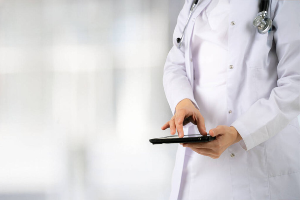 Großaufnahme der Hände und des elektronischen Tablets einer jungen Ärztin oder Wissenschaftlerin im weißen Kittel in der Lobby des Krankenhauses - Foto, Bild