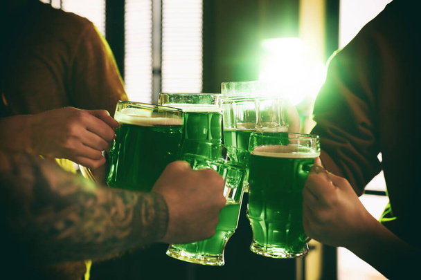Group of friends toasting with green beer in pub, closeup. St. Patrick's Day celebration - Foto, afbeelding