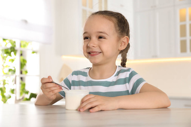 Cute little girl with tasty yogurt at table in kitchen - Foto, afbeelding