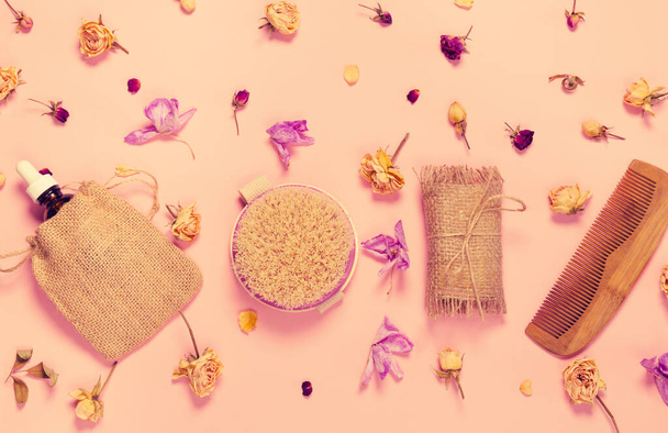 Set of natural soap, aroma oil, wooden comb  and body massage brush with dried rose and orchid buds as a decoration on pastel background. Home spa concept. Beauty rituals theme. - Photo, Image