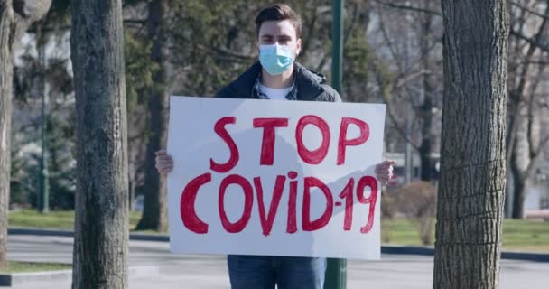 Joven con máscara protectora sosteniendo cartel Stop COVID-19
 - Metraje, vídeo