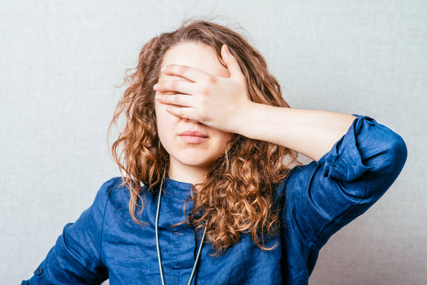 Curly girl covering her eyes with her hand. Gray background. - Фото, изображение