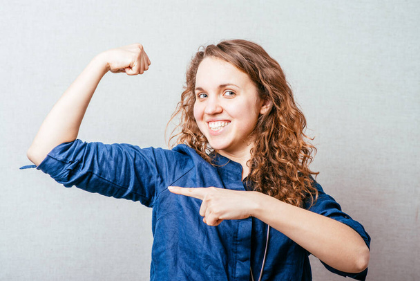 Curly woman showing muscles on his arm. On a gray background. - Фото, зображення