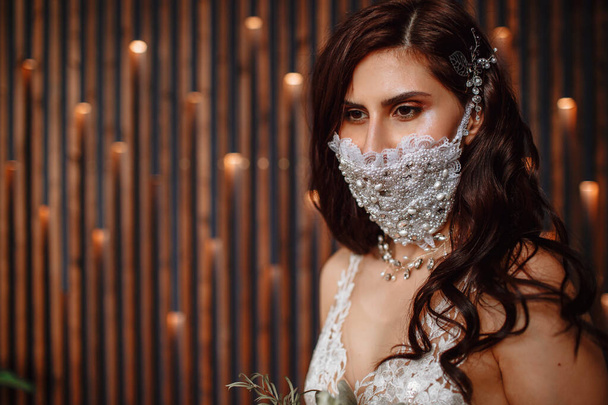 Bride in with a handmade wedding antiviral mask on her face. Wedding bouquet in hand - Foto, imagen