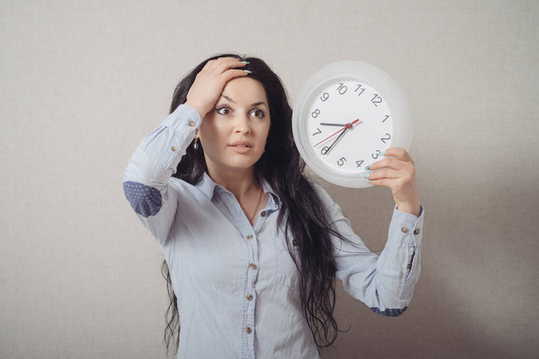 A woman with a wall clock is late. On a gray background. - Foto, afbeelding