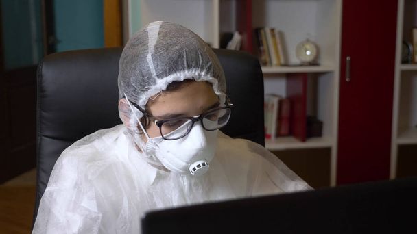 the guy in respirator and protective suit using his laptop while sitting at home - Foto, afbeelding