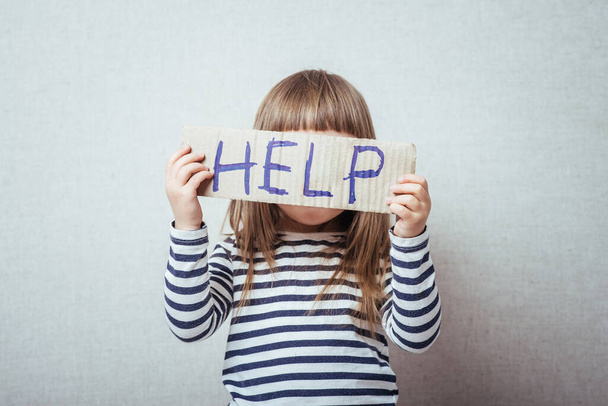 Conceptual image of a sad dejected little girl with a pouting lip standing holding a handwritten HELP sign  - Photo, image