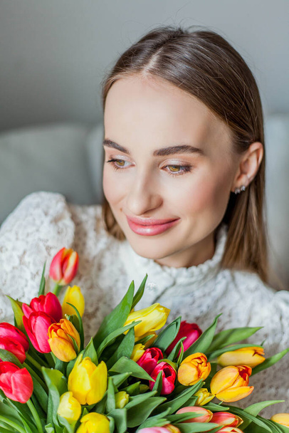 Beautiful young woman holds a multi-colored bouquet of tulips. Spring woman portrait. - Photo, Image