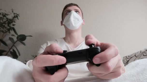 Il concetto di malattia e tempo libero. Un giovane uomo con una maschera medica sul viso che gioca ai videogiochi sul joystick wireless. Starnutisce diverse volte, perde, si arrabbia e abbassa il controller
 - Filmati, video