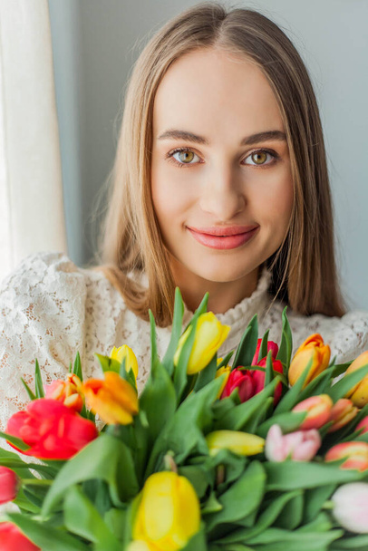 Beautiful young woman holds a multi-colored bouquet of tulips. Spring woman portrait. - Zdjęcie, obraz