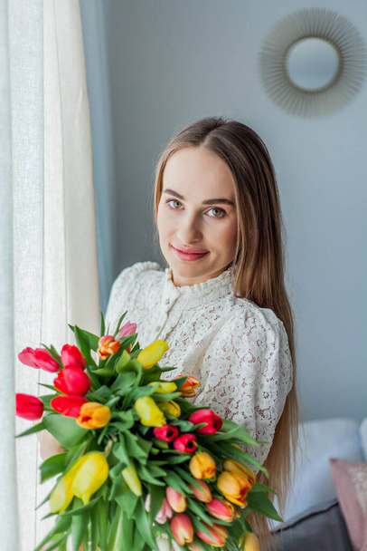 Beautiful young woman holds a multi-colored bouquet of tulips. Spring woman portrait. - Фото, изображение